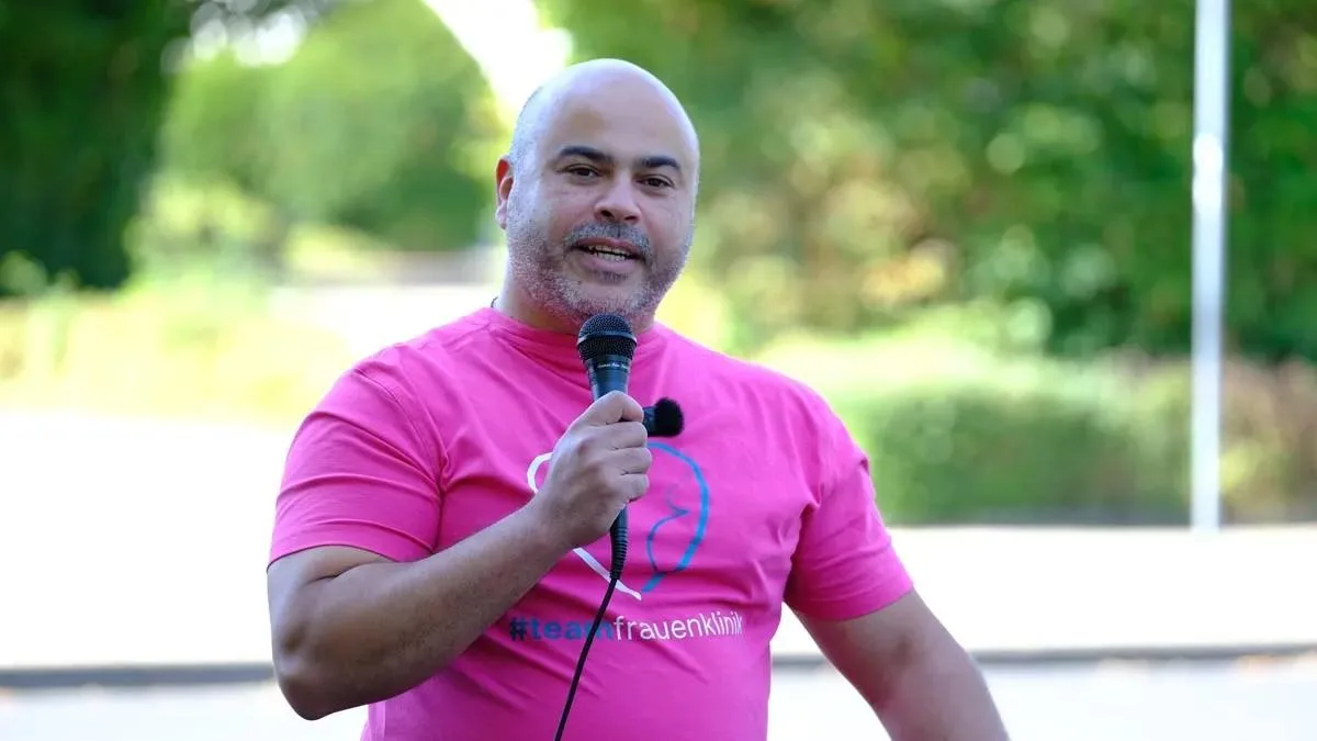 Mohammed Koheil spricht im pinkfarbenen Team-Shirt mit einem Mikrofon zu den Anwesenden.